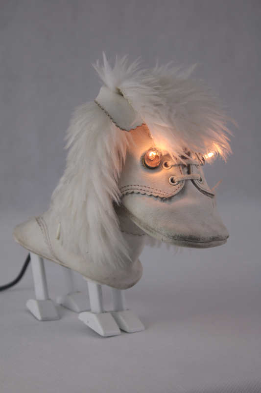 Doblanc Année de création: 2024. Dimensions: 18x 18 x 10 cm. Poids: 0.4 kg. Matières: cuir, métal, fourrure synthétique. Composition: chaussures de bébé, pièce en fonte peinte, tube et fausse fourrure. Alimentation: 12 V 2 E10 . Pièce unique.